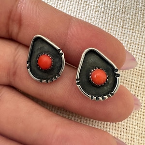 May include: A pair of silver earrings with a black background and a red coral stone in the center.