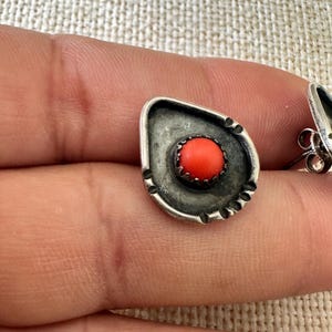 May include: A pair of silver earrings with a coral stone in the center. The earrings are in the shape of a teardrop and have a textured design.