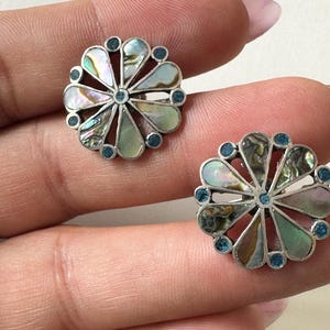 May include: A pair of silver earrings with a flower design. The flowers are made of iridescent abalone shell and have blue accents.