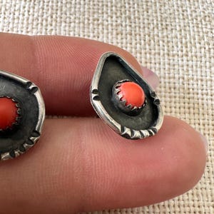 May include: A pair of silver earrings with a coral stone in the center. The earrings are shaped like a teardrop and have a textured design.