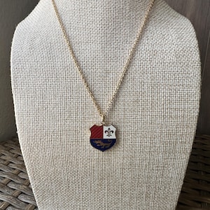 May include: Gold chain necklace with a shield pendant. The shield is red, white, and blue with a gold lion and fleur-de-lis.