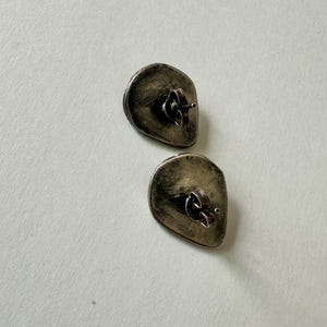 May include: A pair of silver stud earrings with a textured, irregular oval shape.