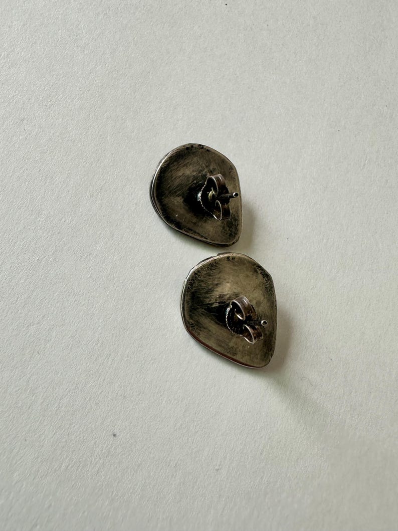 May include: A pair of silver stud earrings with a textured, irregular oval shape.