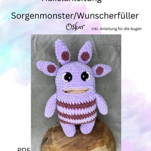 May include: Crochet pattern for a purple worry monster with brown stripes and brown spots. The pattern is called "Oskar" and includes instructions for making the eyes. The pattern is available as a PDF download.