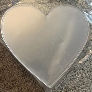 Może przedstawiać: Zbliżenie na przezroczysty, plastikowy przedmiot w kształcie serca, prawdopodobnie forma lub materiał do rękodzieła. Plastik jest półprzezroczysty, a kształt serca jest dobrze zdefiniowany. Przedmiot jest zapakowany w przezroczysty plastik.