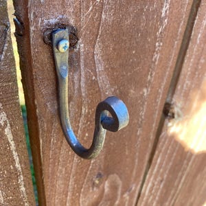 May include: A silver metal hook with a decorative curl at the end is screwed into a wooden surface.