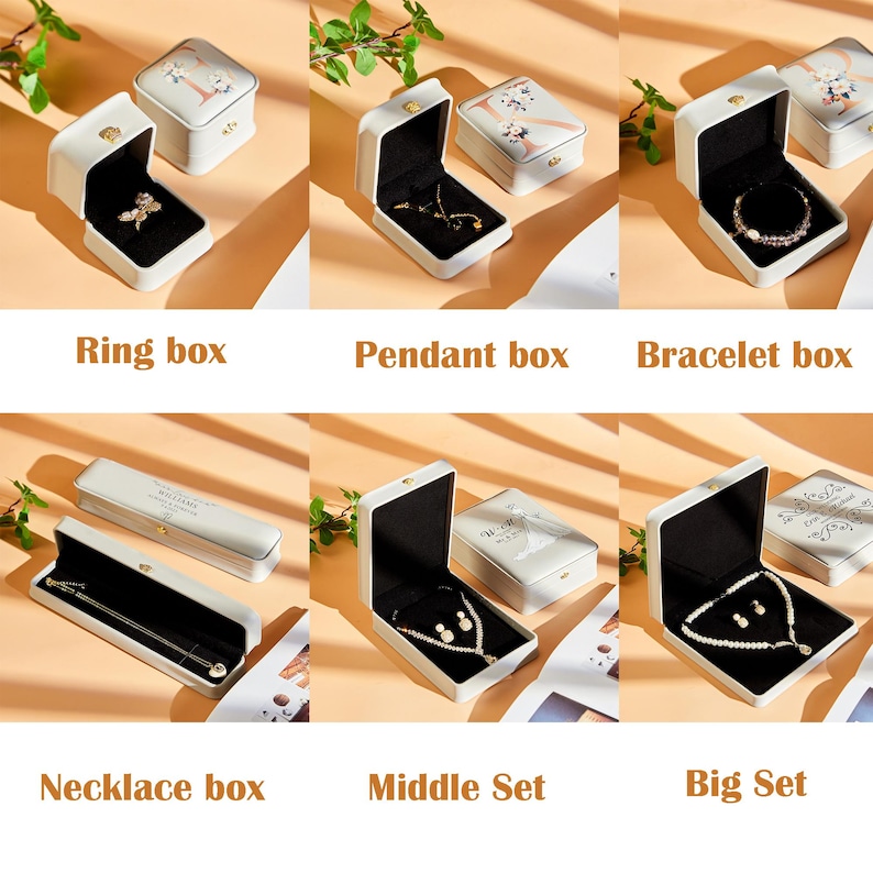May include: A collection of jewelry boxes in various sizes and shapes, including ring, pendant, bracelet, and necklace boxes. The boxes are white with black interiors and feature gold clasps. Some boxes contain jewelry.