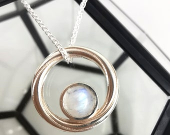 May include: A silver necklace with a round pendant featuring a moonstone set in a circle.
