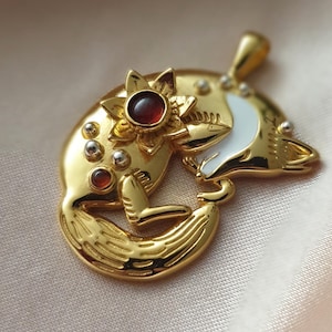 May include: Gold pendant necklace featuring a curled fox design with a white enamel body and a red gemstone accent. The fox is adorned with a gold flower with a red gemstone in the center.