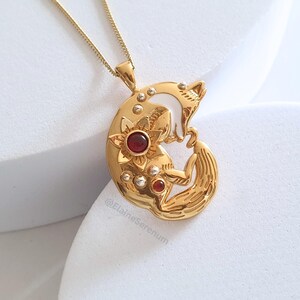 May include: Gold necklace with a pendant featuring a curled fox with red gemstones and white enamel accents. The pendant is detailed with a floral design.