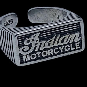 May include: A silver-colored adjustable ring with the words "Indian MOTORCYCLE" in a rectangular design. The ring has a textured band with vertical lines and the number "S925" is stamped on the inside.