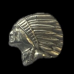 Może przedstawiać: Srebrny pierścionek z metalu z detalicznym profilem osoby tubylczej w nakryciu głowy z piórami. Pierścionek jest wyjątkowym elementem z unikalnym wzorem.