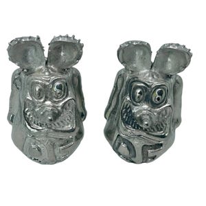 Può includere: Un paio di figurine in metallo color argento a forma di testa di topo. Ogni figurina ha un'espressione da cartone animato con occhi grandi e un ampio sorriso. La parola "Rat" è visibile sul davanti di ogni figurina.