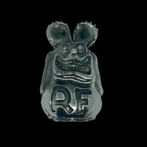 Puede incluir: Un amuleto de plata con forma de rata de dibujos animados con orejas grandes y una sonrisa de dientes. El amuleto tiene las letras "RF" en la parte delantera.
