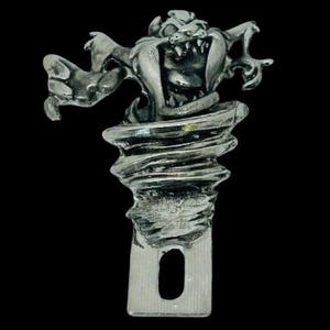 Peut inclure: Un charme en métal argenté représentant un personnage de dessin animé, Taz, des Looney Tunes, émergeant d'un vortex tourbillonnant. Le charme a une boucle en bas pour l'attacher à un collier ou un bracelet.