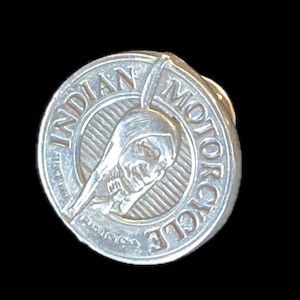 Peut inclure: Épinglette en argent avec le logo Indian Motorcycle. Le logo représente une tête d'Amérindien de profil avec une coiffe à plumes. Les mots "Indian Motorcycle" sont inscrits dans un cercle autour de la tête.