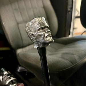 Puede incluir: Una palanca de cambios de color plateado con una escultura detallada de la cabeza de Frankenstein.