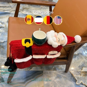 Puede incluir: Un organizador de reposabrazos hecho a mano con temática de Papá Noel, rojo, con cinturón amarillo, ribete blanco y botas negras. Una taza verde y blanca se encuentra encima. El organizador tiene bolsillos y una cara de Papá Noel.
