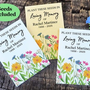May include: Two white cards with colorful flower illustrations and the text "Plant these seeds in loving memory of Rachel Martinez 1956 - 2025". The cards are on a wooden surface.