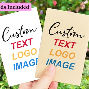 May include: Two blank seed packets with the text "Custom Text Logo Image" printed on them. The packets are made of brown paper and white cardstock. The text is in different colours, including red, yellow, and blue.