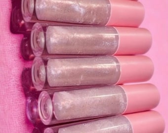 May include: A stack of lip gloss tubes with clear barrels filled with glittery, light-colored gloss. The tubes have pink caps and are arranged against a pink background, creating a cohesive and visually appealing display.