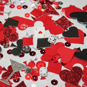 May include: A collection of red, black, and silver playing card and casino-themed confetti. Includes hearts, spades, clubs, diamonds, dice, and sequins. A playing card with the Ace of Hearts is visible.
