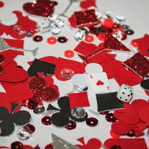 May include: A collection of red, black, and silver playing card-themed confetti, including hearts, spades, diamonds, and clubs. Also includes dice, sequins, and sparkling gems. The Ace of Hearts playing card is visible.