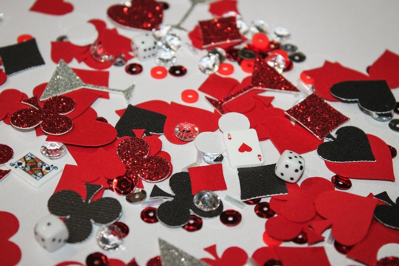 May include: A collection of red, black, and silver playing card-themed confetti, including hearts, spades, diamonds, and clubs. Also includes dice, sequins, and sparkling gems. The Ace of Hearts playing card is visible.