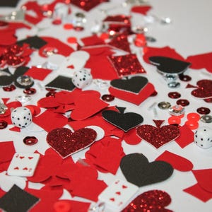 May include: A scattered assortment of red, black, and silver playing card-themed confetti. Includes hearts, spades, diamonds, clubs, dice, and playing cards. Some elements have glitter accents, creating a festive look.