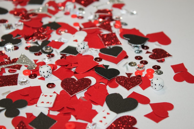 May include: A scattered assortment of red, black, and silver playing card-themed confetti. Includes hearts, spades, diamonds, clubs, dice, and playing cards. Some elements have glitter accents, creating a festive look.