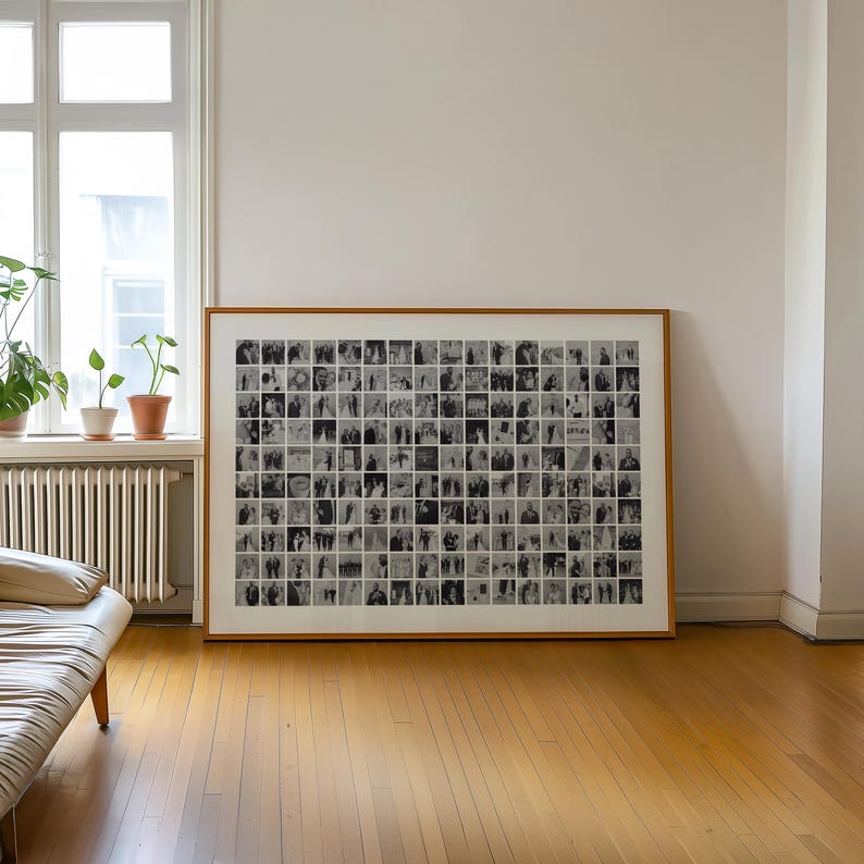 May include: A large framed artwork featuring a grid of small, black and white photographs. The frame is a warm, light brown color. The artwork is displayed on a hardwood floor in a room with a window and a couch.