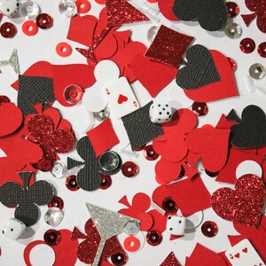 May include: A scattered assortment of red, black, and silver confetti pieces. The confetti includes hearts, diamonds, clubs, and spades, along with dice, playing cards, and martini glass shapes. Some pieces have glitter accents.