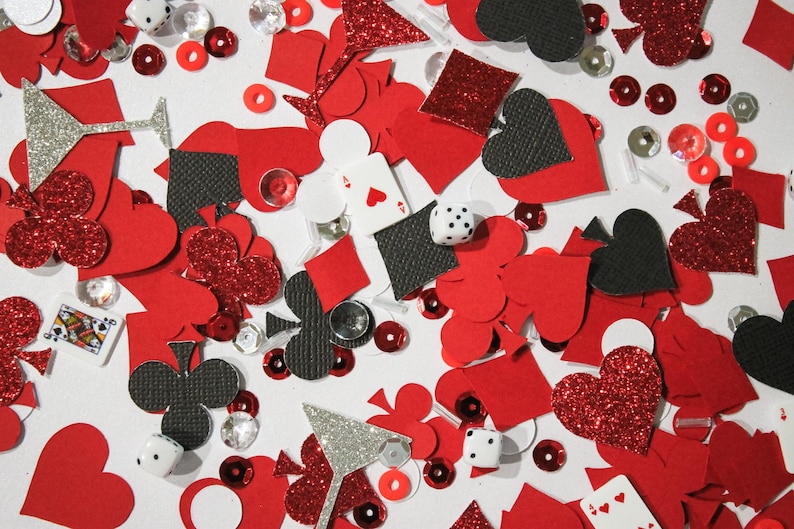 May include: A scattered assortment of red, black, and silver confetti pieces. The confetti includes hearts, diamonds, clubs, and spades, along with dice, playing cards, and martini glass shapes. Some pieces have glitter accents.