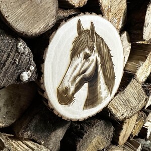 Peut inclure: Plaque en bois rond avec une gravure détaillée d'une tête de cheval. L'œuvre d'art est dans des tons bruns et beiges, montrant le profil du cheval. La plaque est placée sur un fond de bois de chauffage empilé.