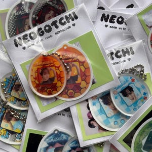 May include: A collection of colorful Tamagotchi keychains with different designs. The keychains are made of clear plastic and feature a variety of characters and images. The keychains are attached to silver chains.