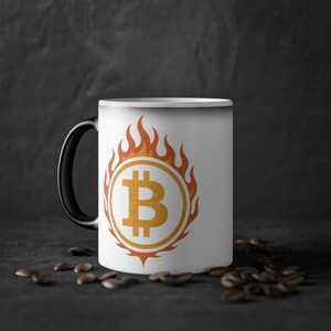May include: White ceramic mug with a black handle. The mug features a graphic of a bitcoin symbol inside a circle with flames around it. The flames are orange and yellow.