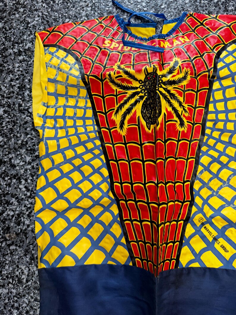 May include: A sleeveless costume top featuring a red and yellow spiderweb pattern with a large black spider graphic in the center. The text SPIDER-MAN is printed near the neckline, and the lower right side includes the text 2001 MARVEL COMICS GROUP.
