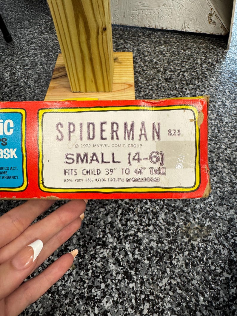 May include: A rectangular red cardboard box for a Spiderman mask, model 823, dated 1972 Marvel Comic Group. The label specifies size small (4-6) for a child 39 inches to 44 inches tall, noting 40% vinyl and 60% rayon material composition.