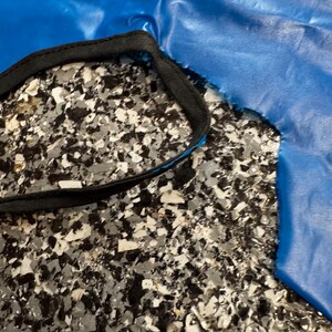 May include: A bright blue fabric piece with a smooth, slightly reflective surface and a jagged, uneven edge. The fabric features a black fabric trim stitched along a curved opening, creating a distinct contrast against the vibrant blue material.