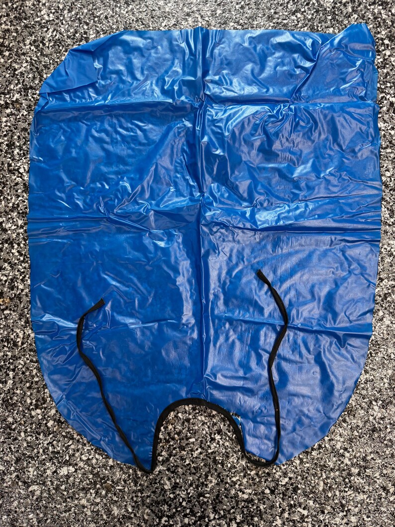 May include: A bright blue, rectangular plastic apron with a smooth, crinkled texture. The apron features a rounded neckline with thin, black fabric ties attached to the sides for securing the garment around the torso during use.