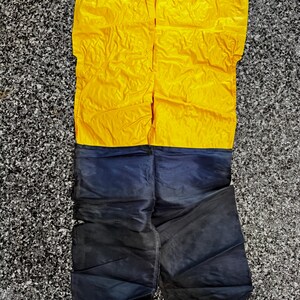 May include: A two-piece garment featuring a bright yellow sleeveless top with thin blue shoulder straps and a pair of dark navy blue pants. The top is solid yellow, while the pants are a deep, dark blue color with visible stitching.