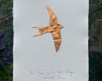 May include: A rectangular piece of white textured paper with deckled edges featuring a metallic copper-colored swallow in flight. Below the bird, the handwritten text reads: The Peace of Wild Things - Wendell Berry, written in black ink.