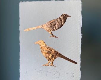 May include: A rectangular piece of white textured paper with deckled edges featuring two metallic copper-colored bird silhouettes. The text "Two for Joy" is handwritten in pencil at the bottom, along with the fraction 1/4 and the signature 9/26.
