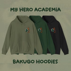 May include: Three hoodies in olive green, dark green, and black. Each features a chest graphic of a green and orange design. The text "MY HERO ACADEMIA" and "BAKUGO HOODIES" are displayed above and below the hoodies.