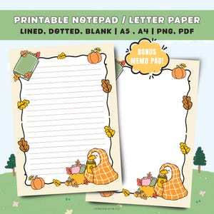 May include: Two printable notepad and letter paper sheets with a cream background, featuring a black border decorated with orange pumpkins and autumn leaves. A cartoon duck wrapped in an orange plaid blanket holds a yellow cup at the bottom.