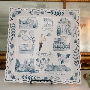 Może przedstawiać: Kwadratowa biała taca ceramiczna z falistymi brzegami, ozdobiona niebieskimi ilustracjami przedstawiającymi różne zabytki, parę oraz napisy, w tym "The Fishers", "Chicago", "D.C.", "St. Paul on the Lake" i "Country Club of Detroit".