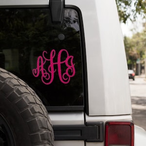 May include: A white car with a pink monogram sticker on the back window. The sticker is a cursive font with the letters "AHS".
