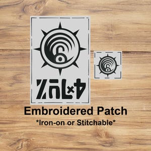 May include: Two grey embroidered patches on a wooden surface. The larger patch has a black circular design with a stylized number 6 and text below. The smaller patch is a miniature version. Text on the larger patch reads "Embroidered Patch *Iron-on or Stitchable*".
