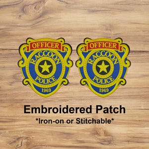 May include: Two embroidered patches with a blue and yellow police badge design. The badge reads "Officer Raccoon Police 1969" with a gold star in the center. The text "Embroidered Patch" and "Iron-on or Stitchable" are below the badges.