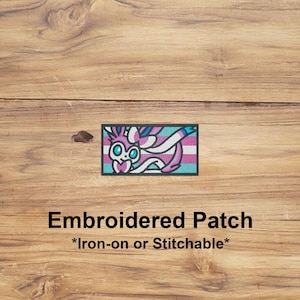 May include: Embroidered patch featuring a stylized creature with pink, white, blue, and teal colors. The patch has a rectangular shape with a teal border. Text on the image reads "Embroidered Patch *Iron-on or Stitchable*".